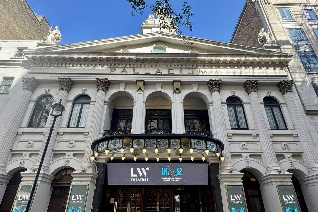 The impressive façade of LW Theatres venue 'The London Palladium', featuring classical architectural elements including columns and statues. Digital signage above the entrance is displaying "LW Theatres" and "Nordoff and Robbins Music Therapy."